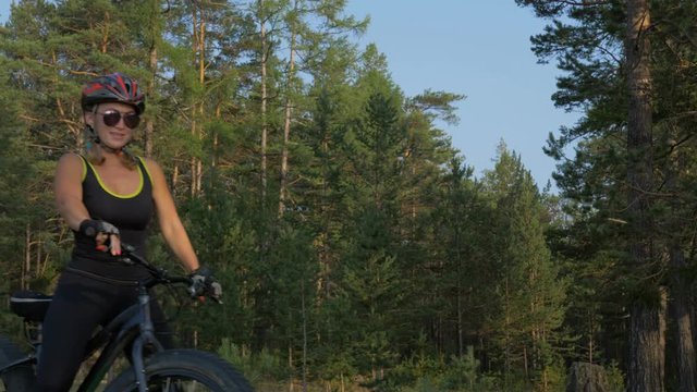 Fat bike also called fatbike or fat-tire bike in summer riding in the forest. Beautiful girl and her bicycle in the forest. She comes from the forest and gets off the bike.