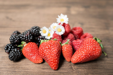 Strawberries and berries adorned with field daisies, a prelude of summer, placed on an old table. It is a good and fresh fruit that is very healthy and contains few sugars.
