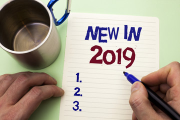 Writing note showing  New In 2019. Business photo showcasing Fresh Era Latest Year Period Season Annual Coming Modern written by Man on Notebook Paper Holding Marker on plain background Cup.
