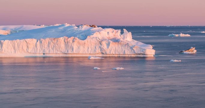 Arctic nature landscape with icebergs in Greenland icefjord with midnight sun sunset / sunrise in the horizon. Aerial drone footage video of ice. Ilulissat Icefjord with icebergs from glacier.