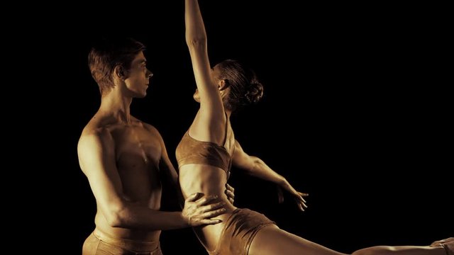 Professional, emotional ballet dancers on dark scene performed by sexual couple with golden body art.Shining gold skin.Pair depicts love and passion on stage Slow motion.