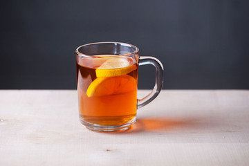 Glass mug with tea and lemon on a dark gray background. Wood surface