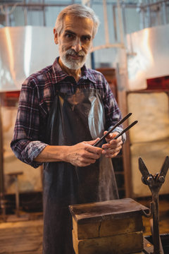 Glassblower holding tongs at glassblowing factory