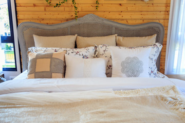 beautiful pillows on a bed with wooden wall and blinds in bedroom.