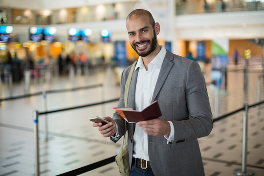 Smiling businessman holding a boarding pass and checking his mobile phone