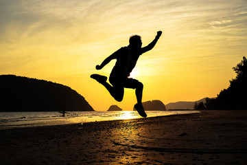 Fototapeta na wymiar man traveler jumping on the beach when sunrise on vacation.silhouette concept.