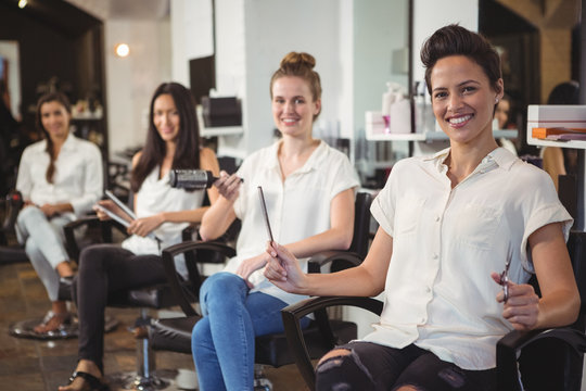 Smiling hairdressers sitting on chair in salon