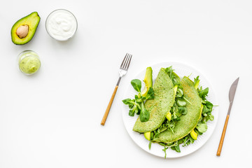 Spinach pancakes with spinach leaves and avocado slices on plate on white background top view copy space