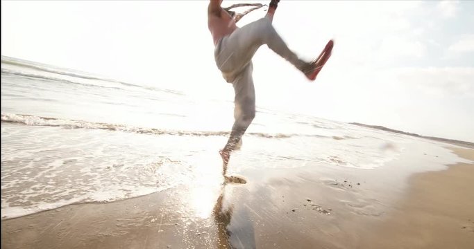 Young muscular man doing capoeira backflip on the beach