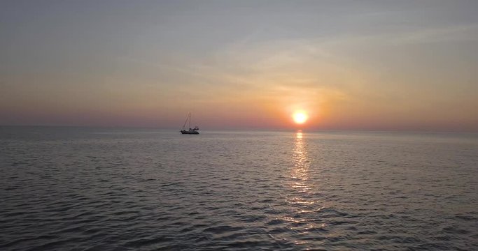 Gliding drone shot of beautiful tropical sunset and a lone sailboat in the ocean