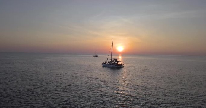 Tourists on a sailboat under astonishing tropical sunset. Gliding drone shot.