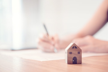 Close up wooden toy house with Woman signs a purchase contract or mortgage for a home, Real estate...