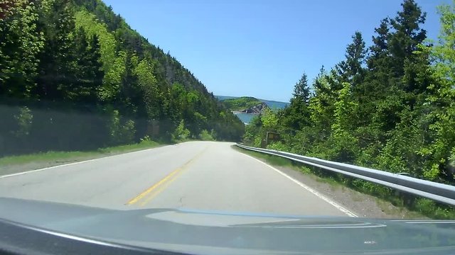 Vehicle drives down hill and around corners to reveal the ocean. Shot from the dash of a vehicle driving on the Cabot Trail on Cape Breton in Nova Scotia, Canada.