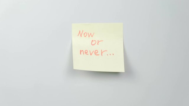 Closeup woman's hands stick yellow sticker paper sheets with words now or never.