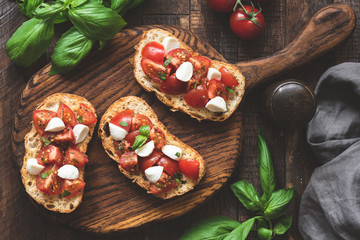 Italian bruschetta antipasti with tomatoes, mozzarella cheese and basil on wooden board. Top view, toned image - obrazy, fototapety, plakaty