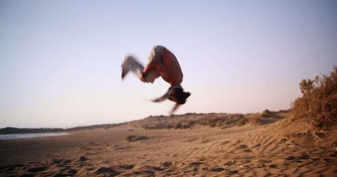 Young muscular man doing parkour backflip jump on beach sand