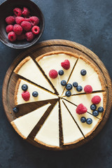 Classical cheesecake with fresh berries on wooden board cut into slices. Top view with copy space for text. Toned image