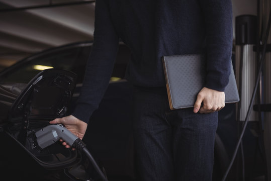 Mid section of man holding organizer while charging electric car