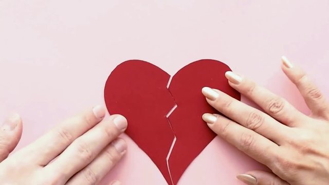 Male and female hand combine together two parts of broken heart, concept. The female hand collects the heart torn to pieces