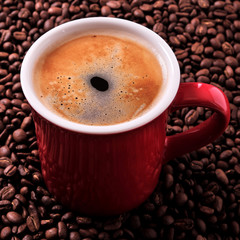 Red coffee mug filled full with espresso americano closeup against a background of scattered dark roasted beans photo