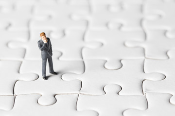 Miniature businessman stand on white jigsaw. One jigsaw are missing from board. Business vision concept.