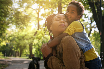 African American mother and her daughter enjoying in park together and hugging.