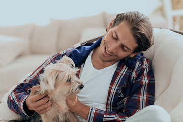 handsome guy stroking his dog while sitting in a large armchair.