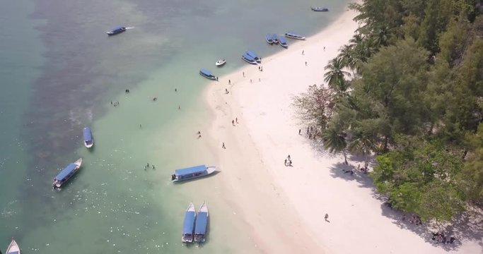 Cinematic drone shot of tourists walking on the shores in a tropical island