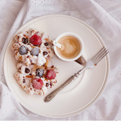 Cup of black coffee and homemade belgian waffles with berries and icing sugar on plate on bed. Good Morning dessert background. Top view.
