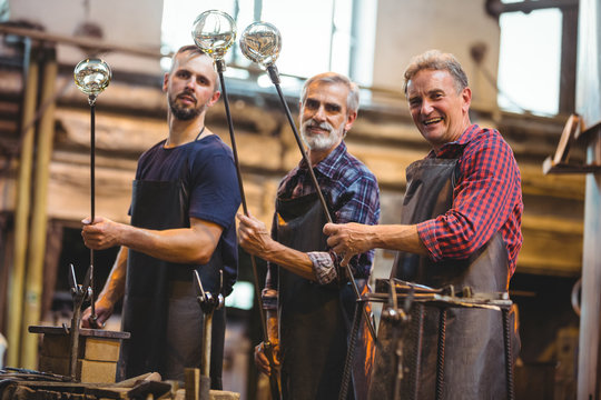 Portrait of team of glassblowers shaping a glass on the blowpipe