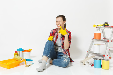Fun pretty woman in casual clothes sitting on floor with yellow gloves, instruments for renovation apartment isolated on white background. Wallpaper accessories for painting tools. Repair home concept