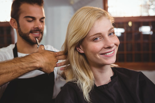 Smiling female getting her hair trimmed with scissor