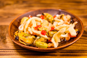 Ceramic plate with different sea food and olives on wooden table