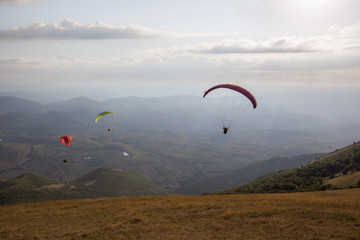 Some colorful paragliders flying over Monte Cucco (Umbria, Italy), with some faint sunrays.