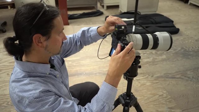 Steadicam to the left closeup on photographer as he adjusts light levels on top of the camera and takes photos.