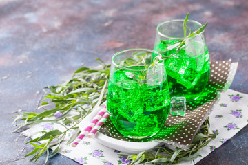 Drink from an estragon with ice in a glass on a table. Selective focus. Copy space