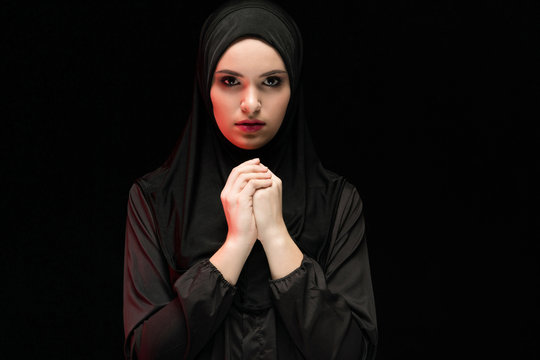 Beautiful young woman wearing black hijab as conservative fashion concept on black background holding hand on hand