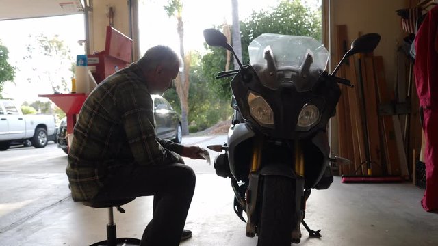 Wide dolly shot of retired man cleaning his motorcycle in the garage