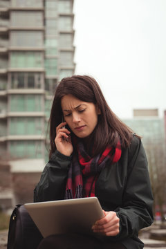 Woman holding tablet while talking on mobile phone