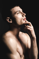 Side view pensive young man with attractive body. He keeping chin by hand. Dreaminess concept