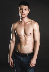 Fototapeta premium Portrait of serene young bare-chested man isolated on dark background. Calm guy with attractive body concept