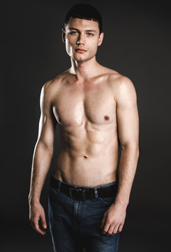 Portrait of serene young bare-chested man isolated on dark background. Calm guy with attractive body concept