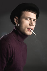 Portrait of annoyed male smoking cigarette while isolated on dark background. Displeasure concept