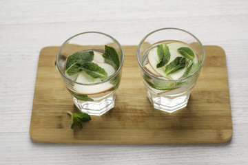 glass with water, apples and mint on a wooden board on a white background.