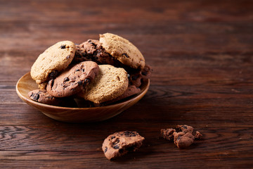 Side view of chocolate chip cookies on a wooden plate over rustic background, selective focus