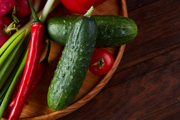 Wooden plate with vegetables for a vegetarian salad on rustic wooden background, close-up, selective focus