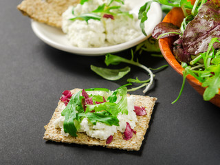 Crisp bread with mix of fresh greens and cream cheese on a black background. Dietary dish