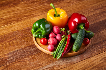 Wooden plate with vegetables for a vegetarian salad on rustic wooden background, close-up, selective focus