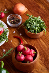 Fresh red radish in wooden bowl among plates with vegetables, herbs and spicies, top view, selective focus.