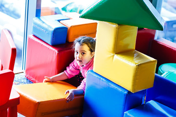 girl playing on the covered Playground on the trampoline with soft foam multi-colored cubes. the concept of childhood.